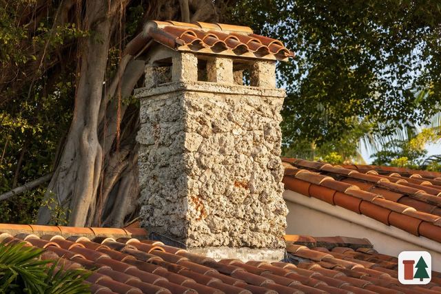 Coral rock chimney with a barrel-tile cap beside a banyan